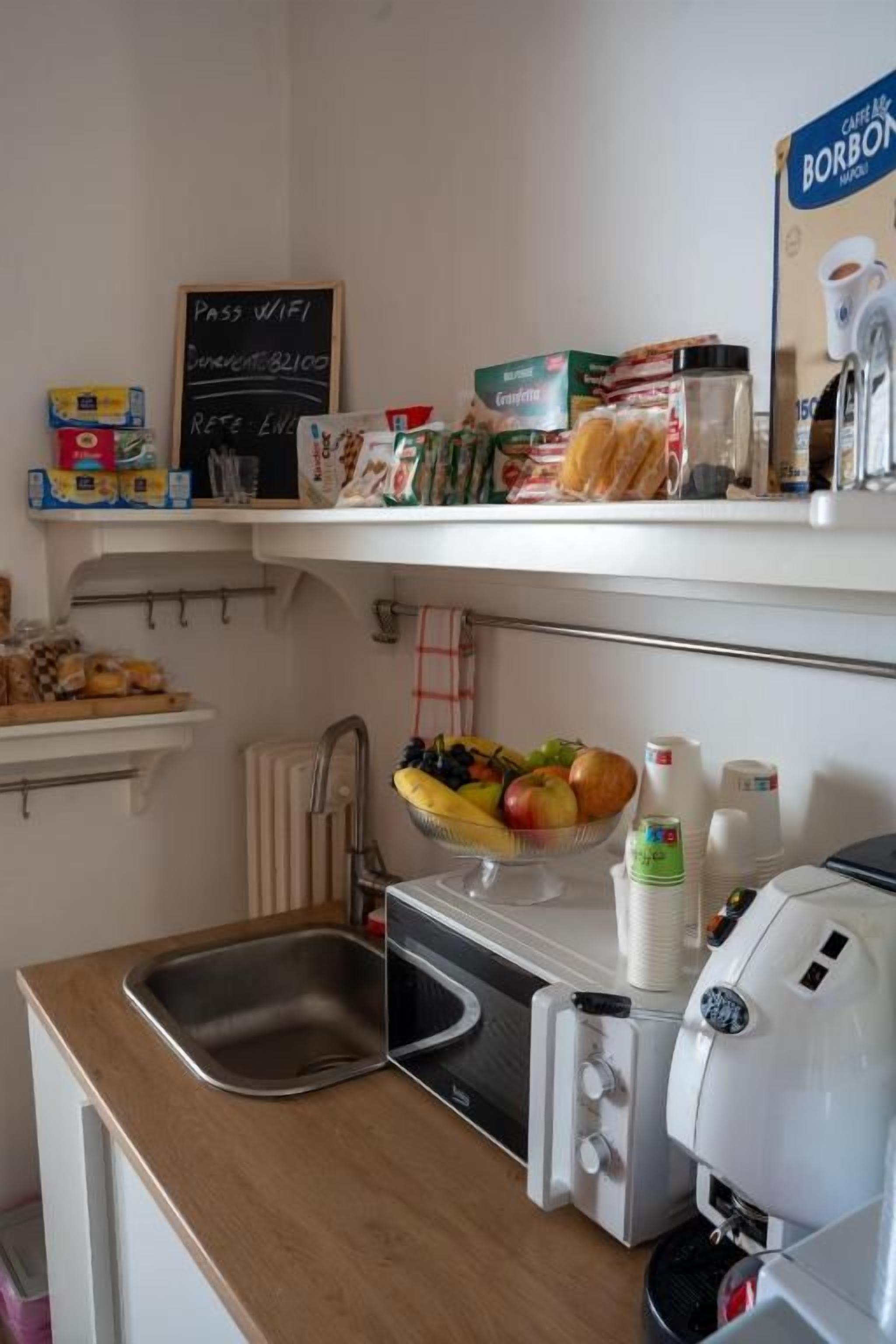Una cocina con microondas, tostadora y cafetera. Hay un bol de fruta en la encimera y varios alimentos en la despensa.