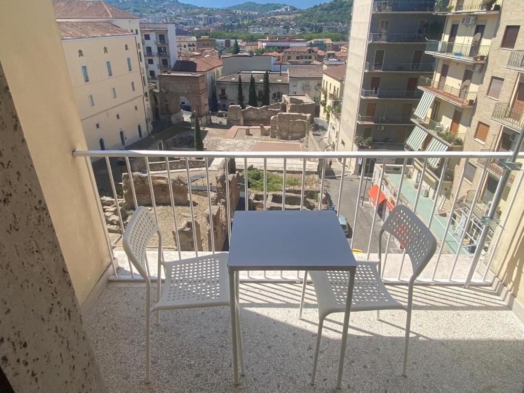 Uma varanda com mesa e duas cadeiras, com vista para uma cidade histórica com edifícios e ruínas.