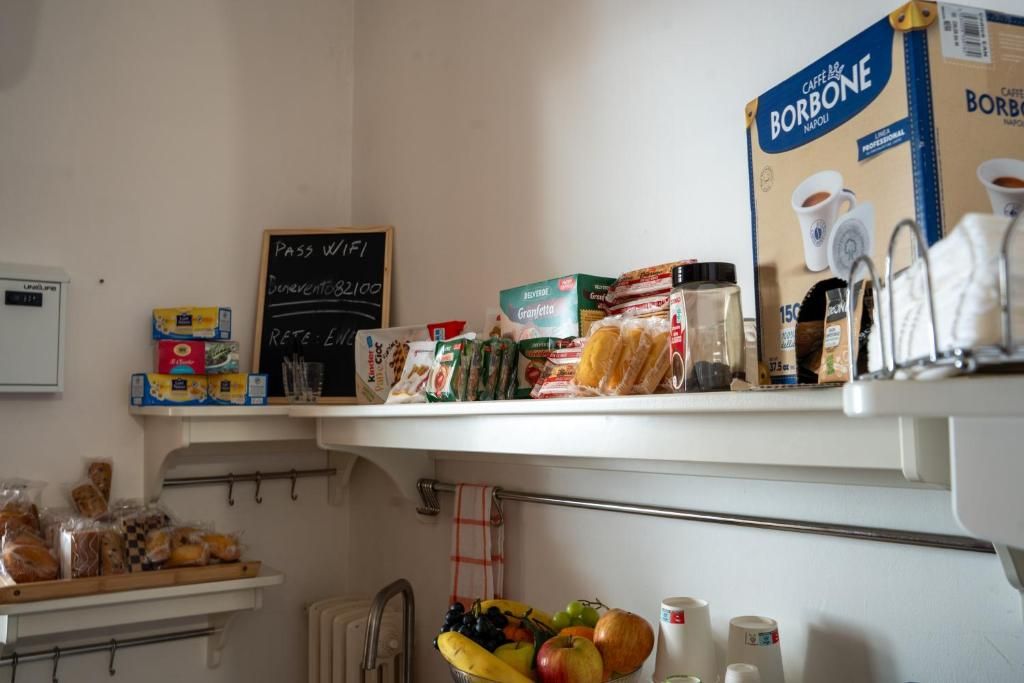 Cozinha com prateleiras repletas de alimentos diversos, uma lousa com anotações manuscritas e uma caixa de café.