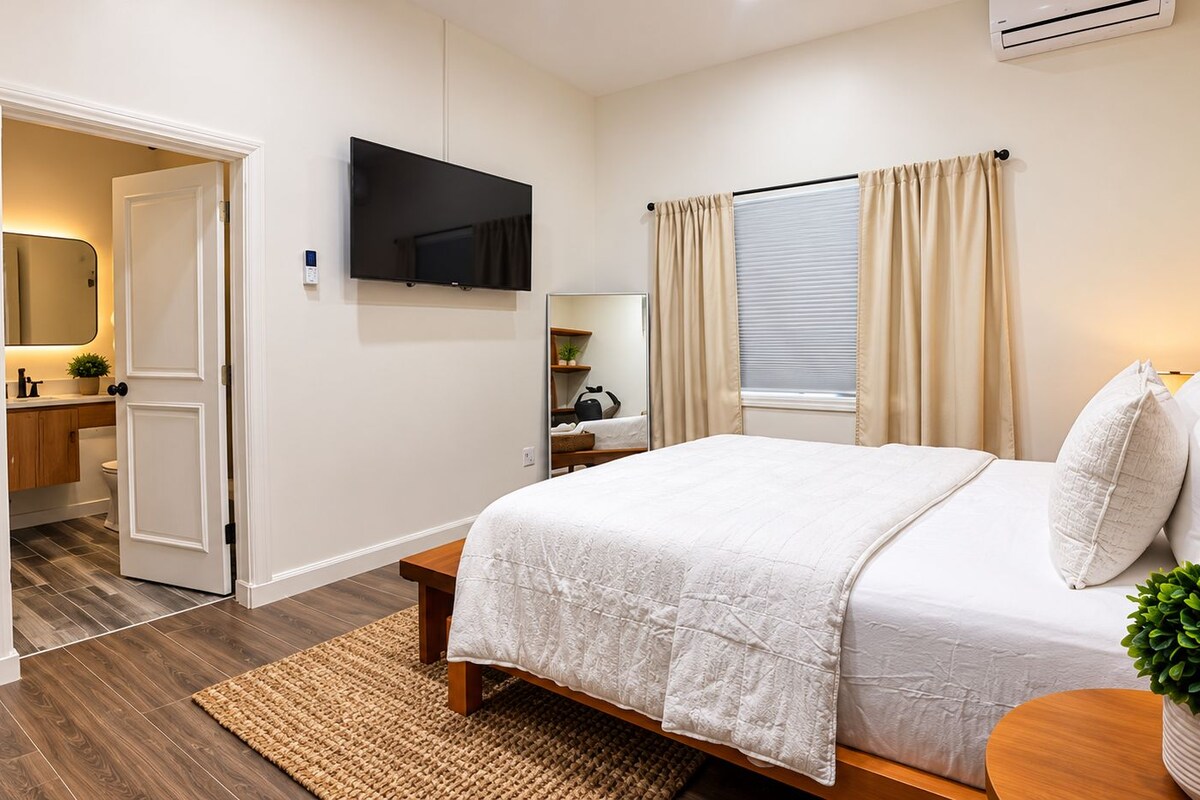 Ein Schlafzimmer mit einem Bett, einem Nachttisch, einem Spiegel, einem Fernseher und einem Fenster mit Vorhängen.