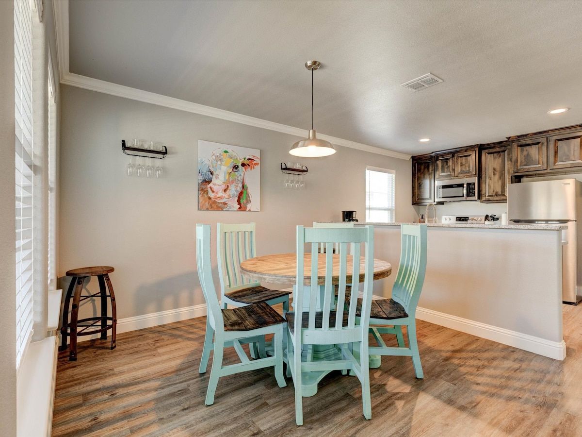 A kitchen with a dining area, wooden flooring, and a hanging light fixture.