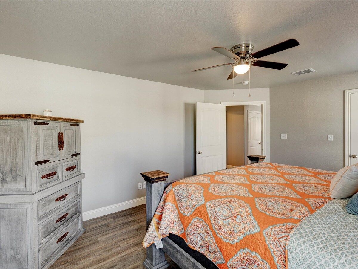 A bedroom with a bed, a dresser, a ceiling fan, and a door leading to another room.