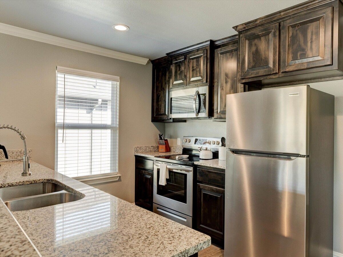 A kitchen with dark wooden cabinets, stainless steel appliances, a granite countertop, and a window with blinds.