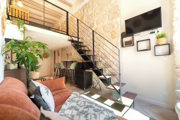 A modern living space with a staircase, a sofa, a dining area, and a TV mounted on the wall. - New Listing (Nice)