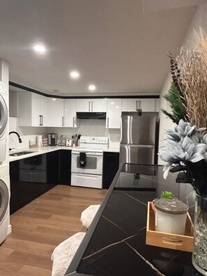 Une cuisine moderne avec des meubles blancs, un réfrigérateur en acier inoxydable et un plan de travail noir.