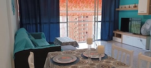 Un comedor con una mesa para dos, un sofá y vistas a un edificio a través de una ventana.