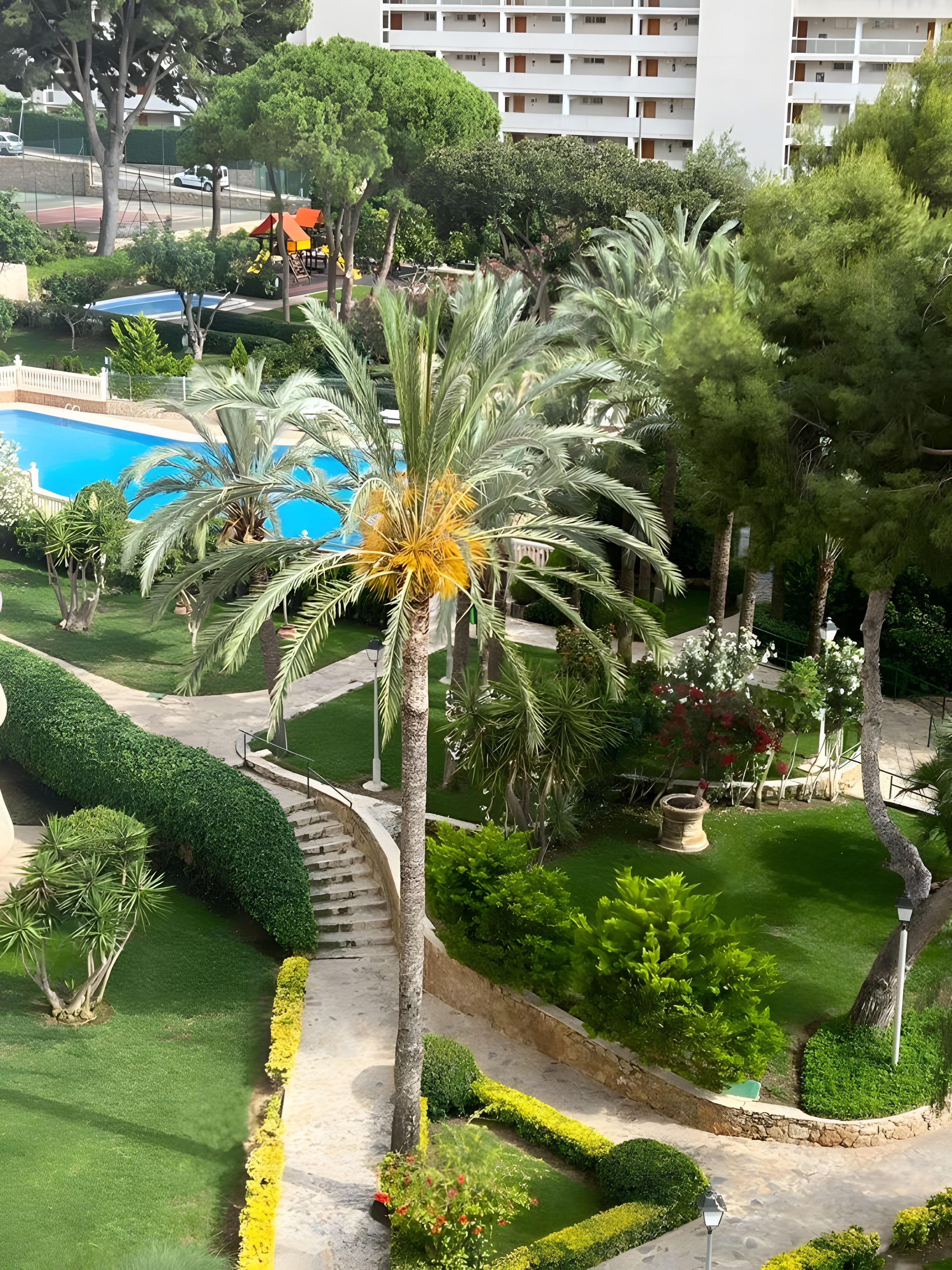 Uma área ajardinada com piscina, palmeiras e um jardim bem cuidado.