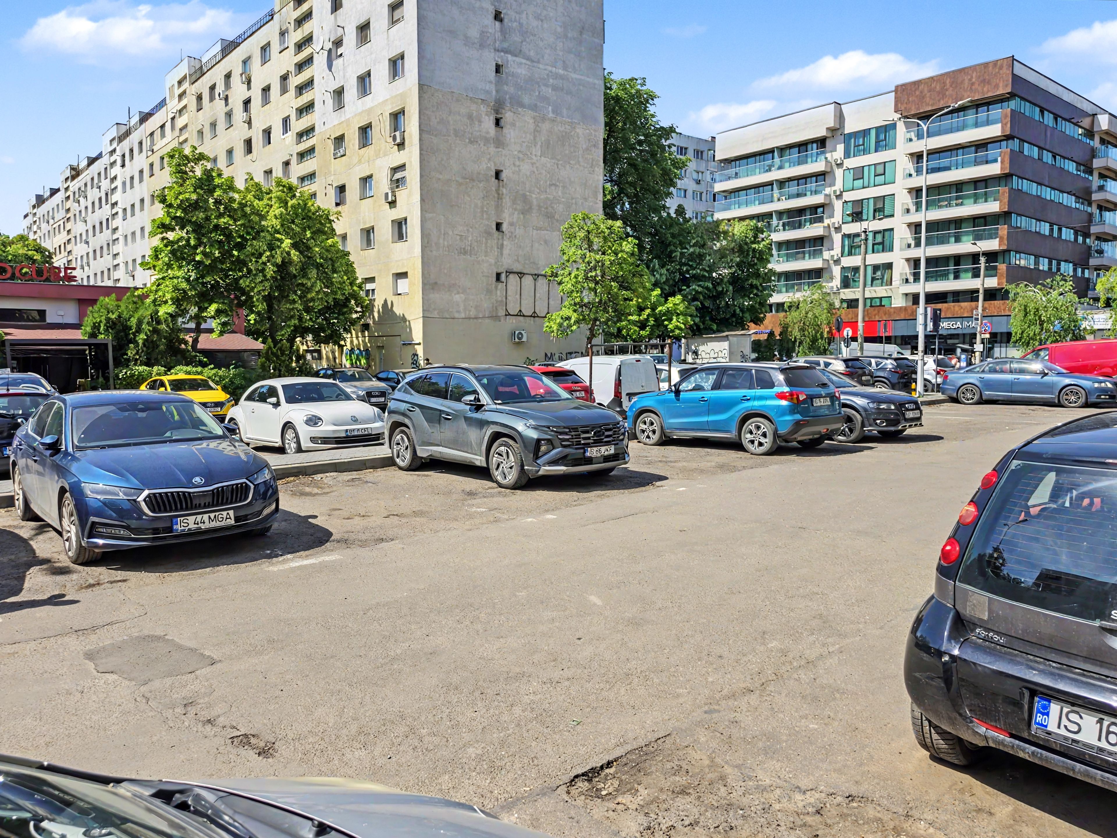 Un parking où sont garées différentes voitures, un immeuble de grande hauteur et un bâtiment à plusieurs étages doté de grandes fenêtres.