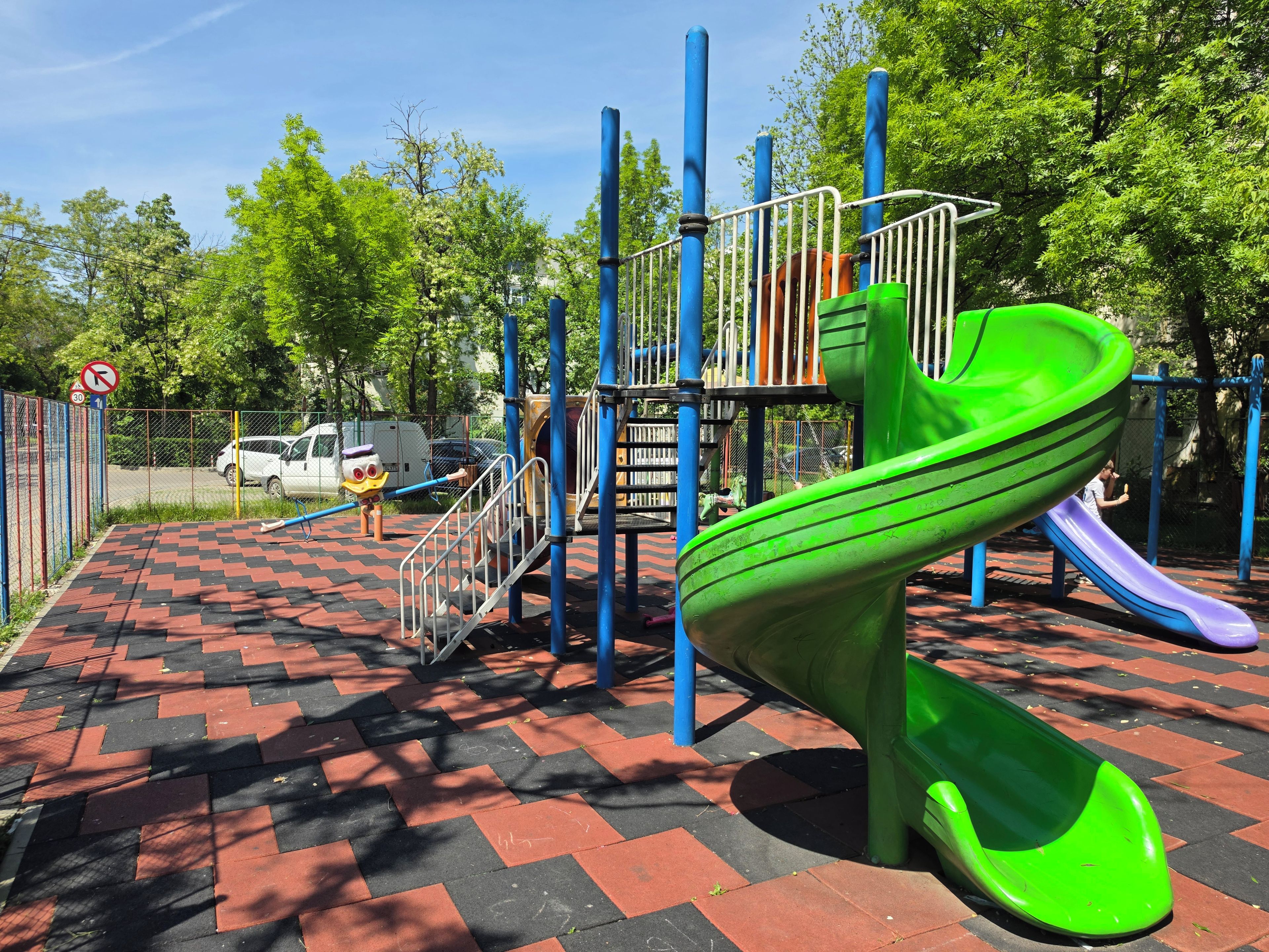 Une aire de jeux avec un toboggan vert et un sol à carreaux rouges et noirs.
