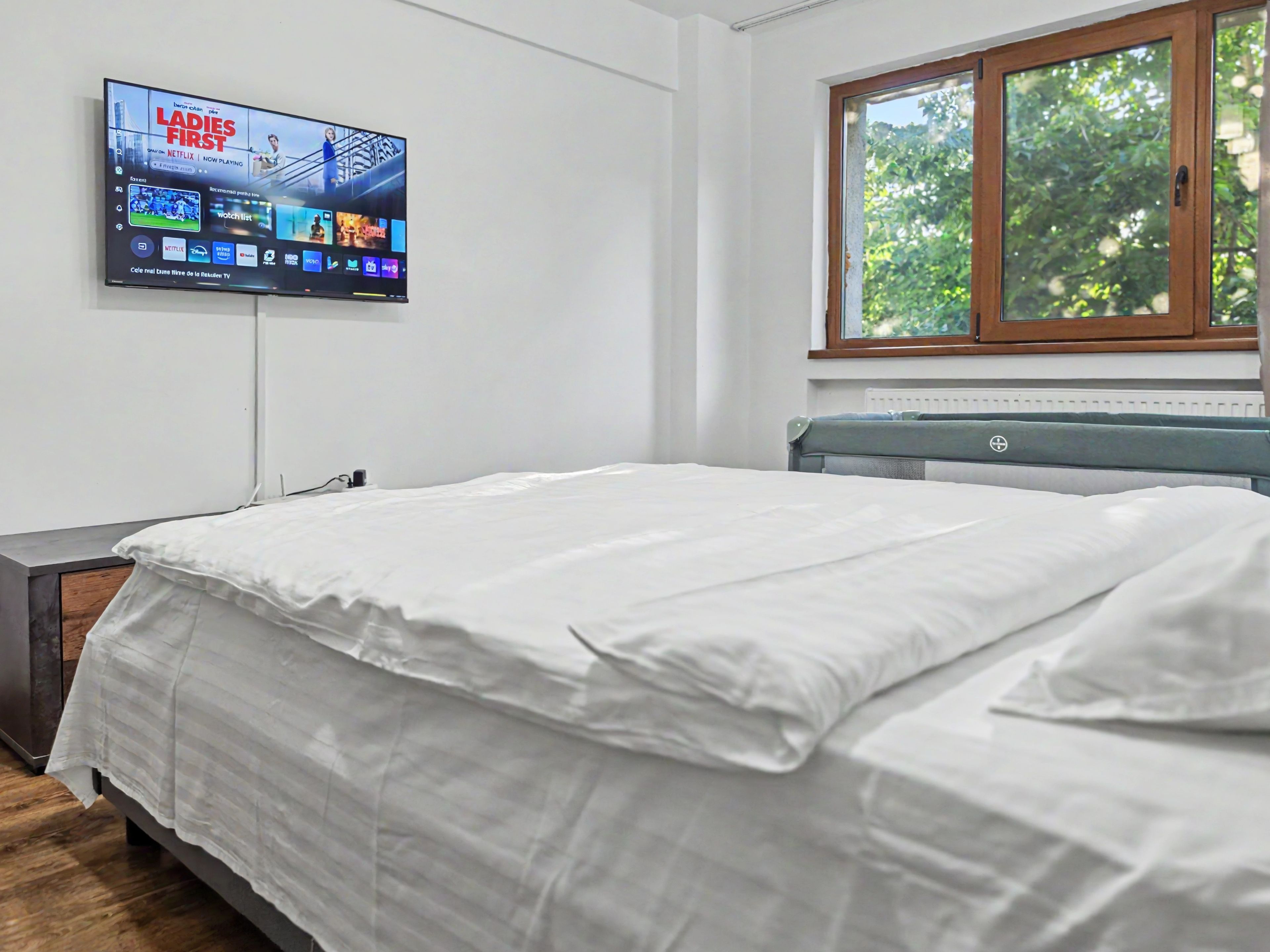 Une chambre avec un lit, un téléviseur fixé au mur et une fenêtre donnant sur un paysage verdoyant.