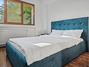 A bedroom with a large bed, a window with a view of trees, a radiator, and a nightstand with a lamp. - Konstanzer 2 - Cozy Apt - Palas Mall  (Iași)