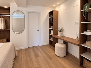 Een slaapkamer met een bed, een kledingkast, een spiegel en een plank met boeken en een plant.