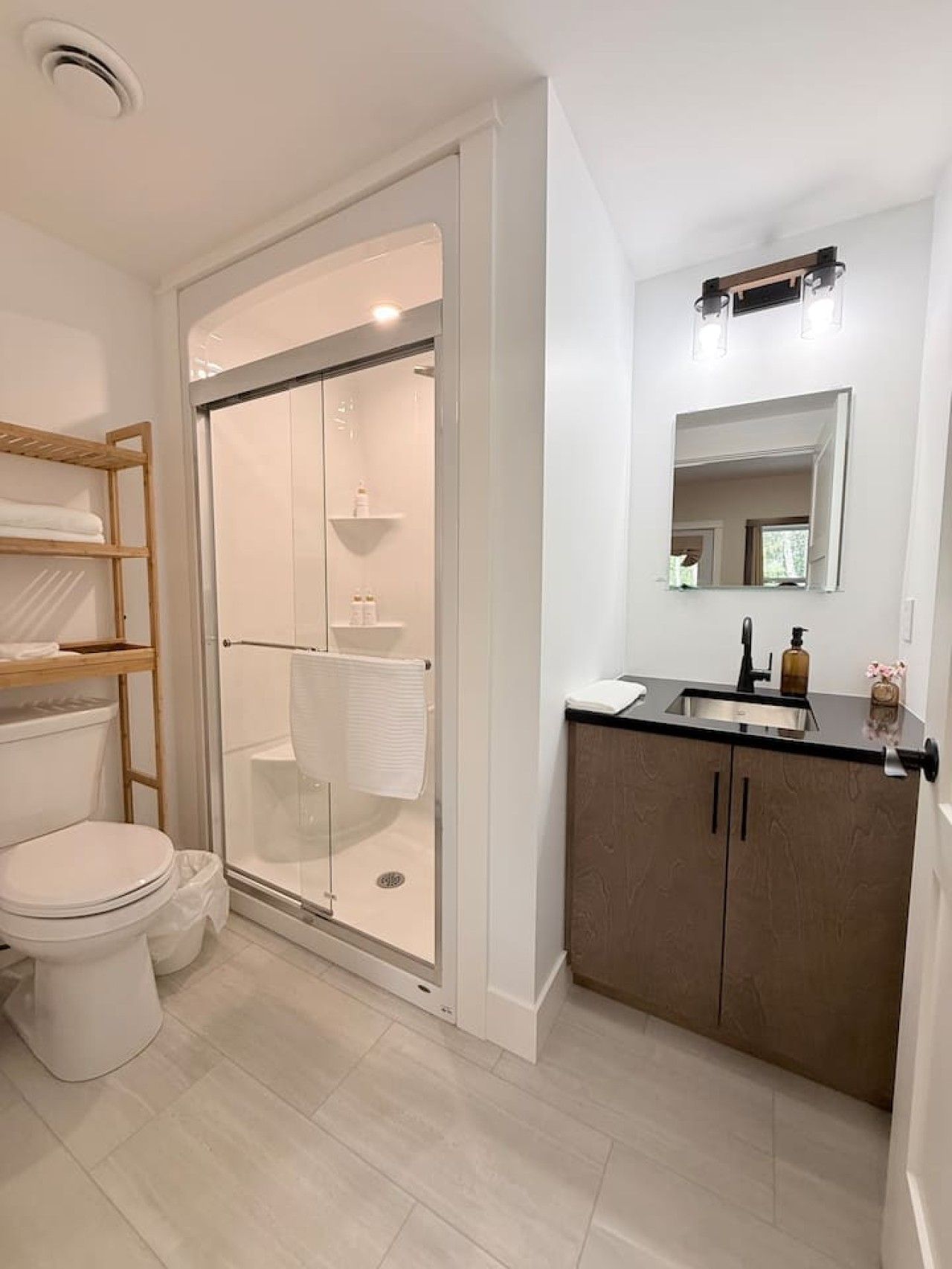 Een moderne badkamer met een douchecabine van glas, een toilet, een wastafel met spiegel en een houten plank.