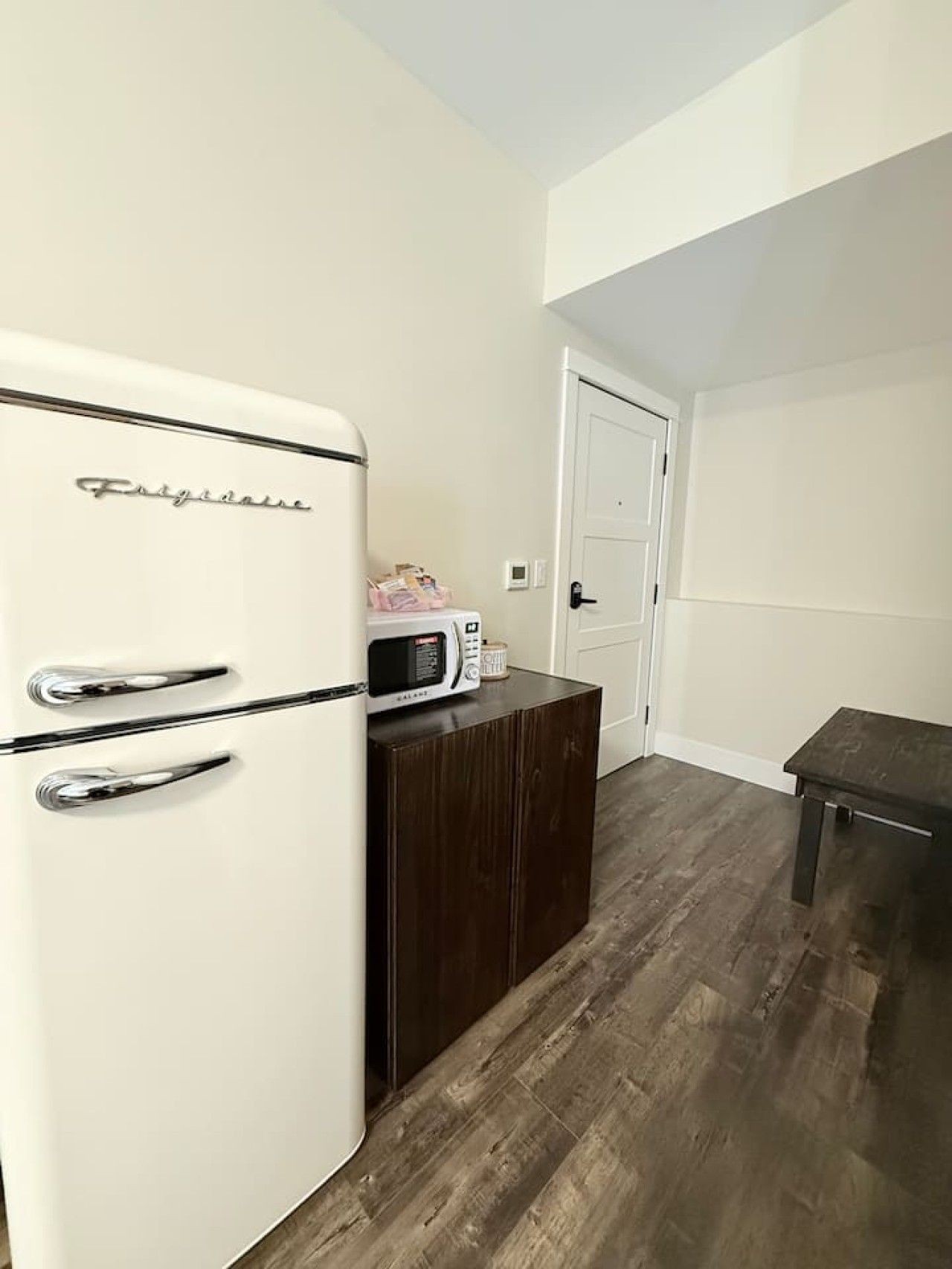 A compact kitchen with a white refrigerator, a microwave, and a small wooden table.
