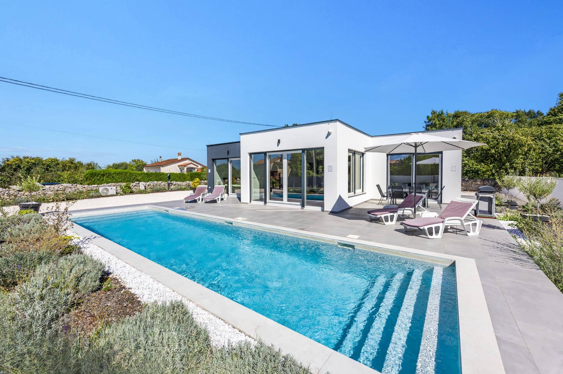Une maison moderne dotée d’une piscine, d’un espace salon extérieur et d’un jardin.