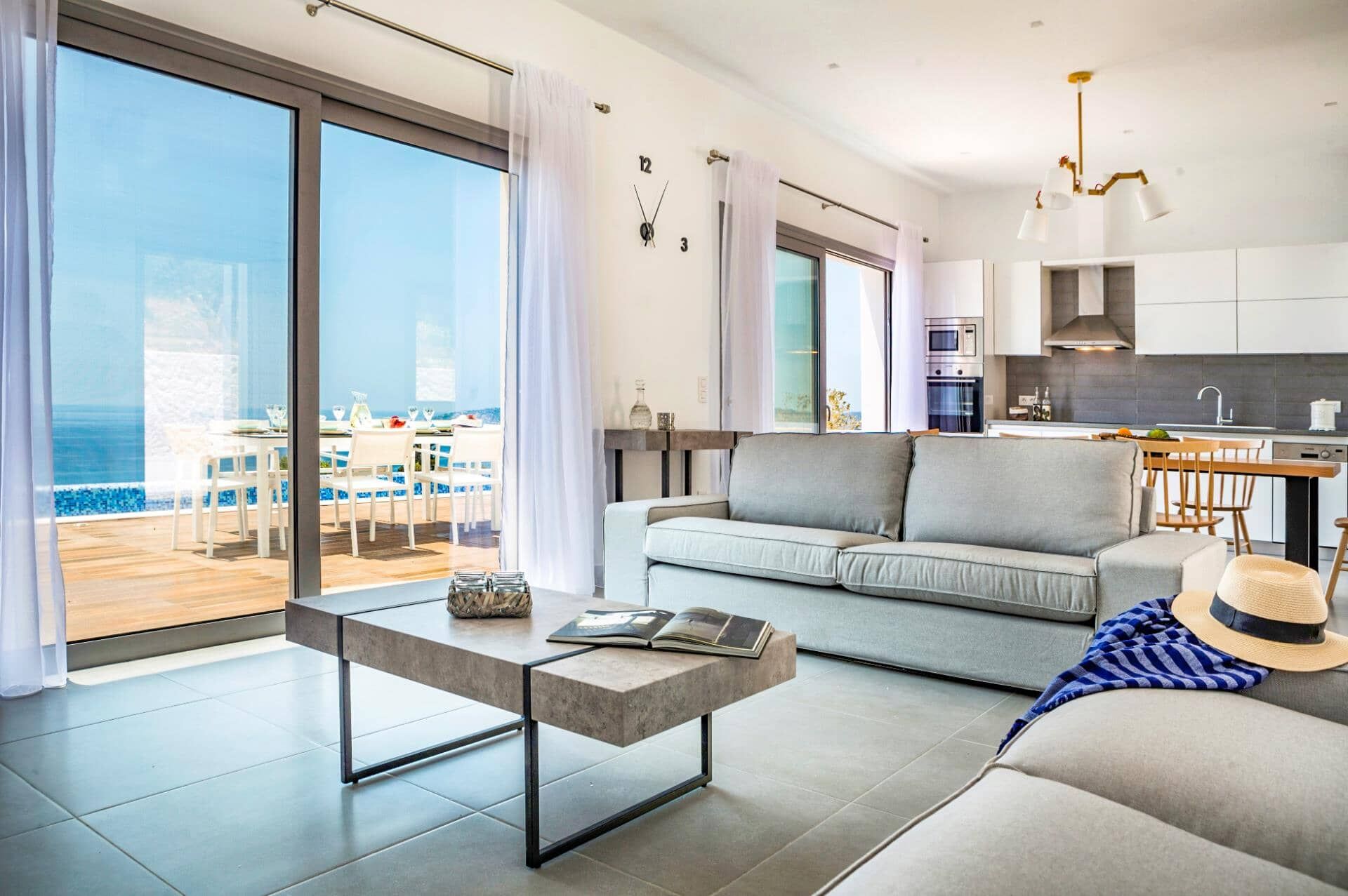 A modern living room with a sofa, a coffee table, and a view of the sea through large windows.