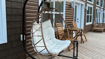 Une terrasse en bois avec un fauteuil suspendu et une table, un bâtiment doté de grandes fenêtres et une porte.