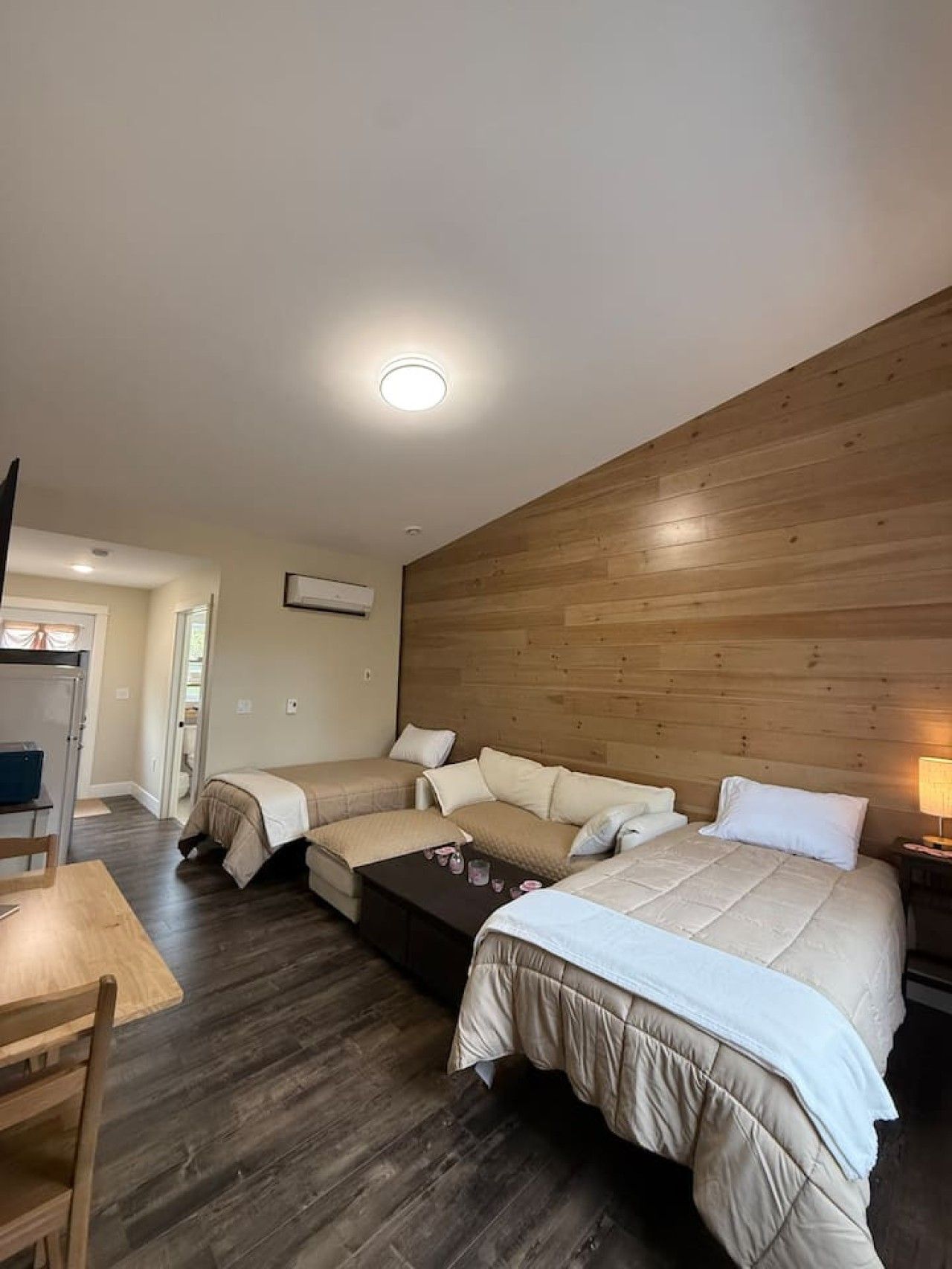 Une chambre d’hôtel avec une tête de lit en bois, un canapé, un lit, un bureau et une chaise.