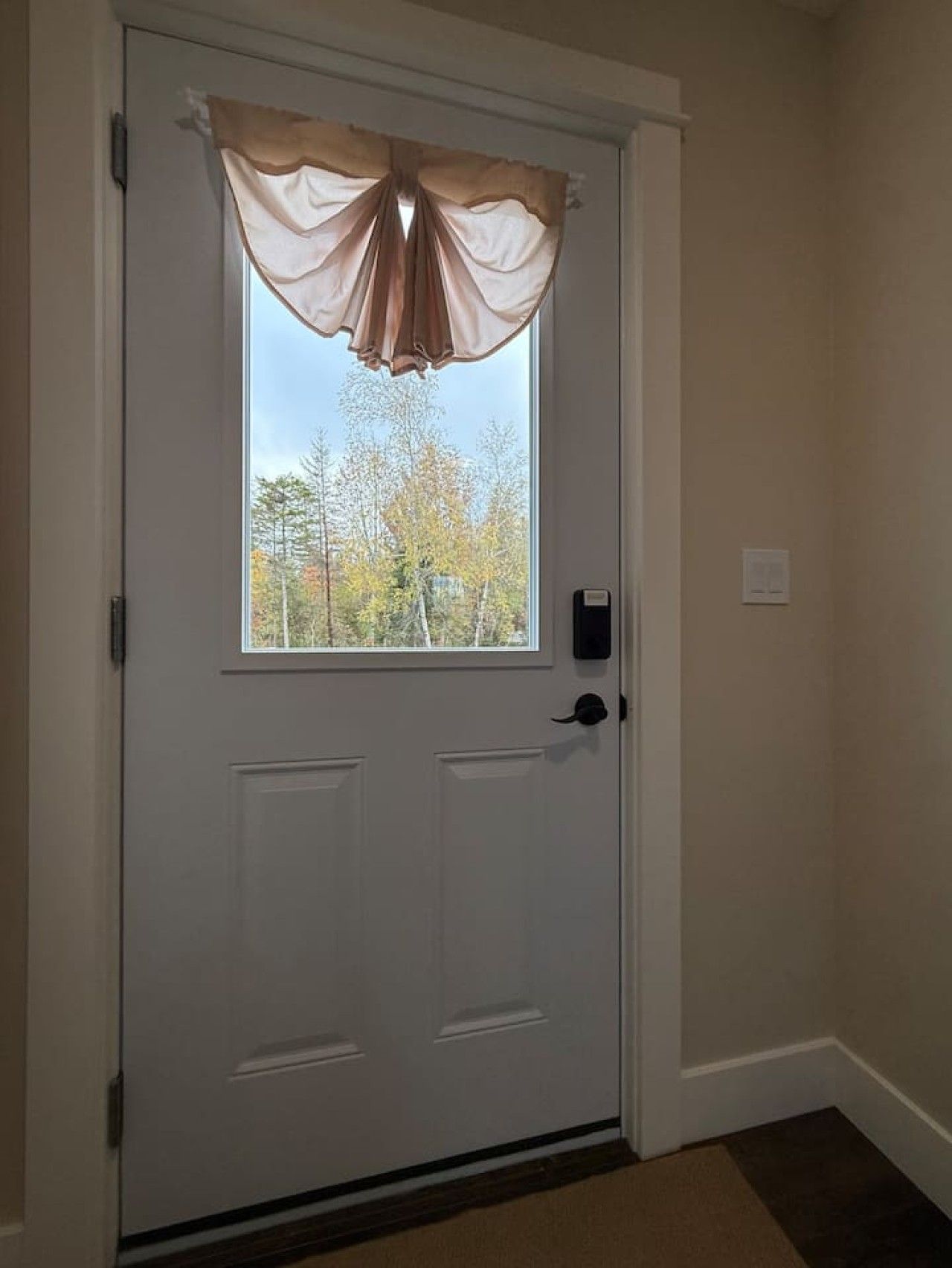 Une porte blanche avec une fenêtre, un carillon et un interphone fixé au mur.