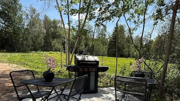 Une terrasse extérieure avec un barbecue, deux chaises en métal et une table.