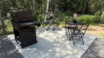 An outdoor grill area with a table and chairs, surrounded by trees.