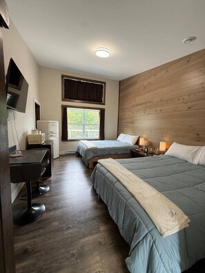 Una habitación de hotel con dos camas, un escritorio, un televisor y una ventana con cortinas.