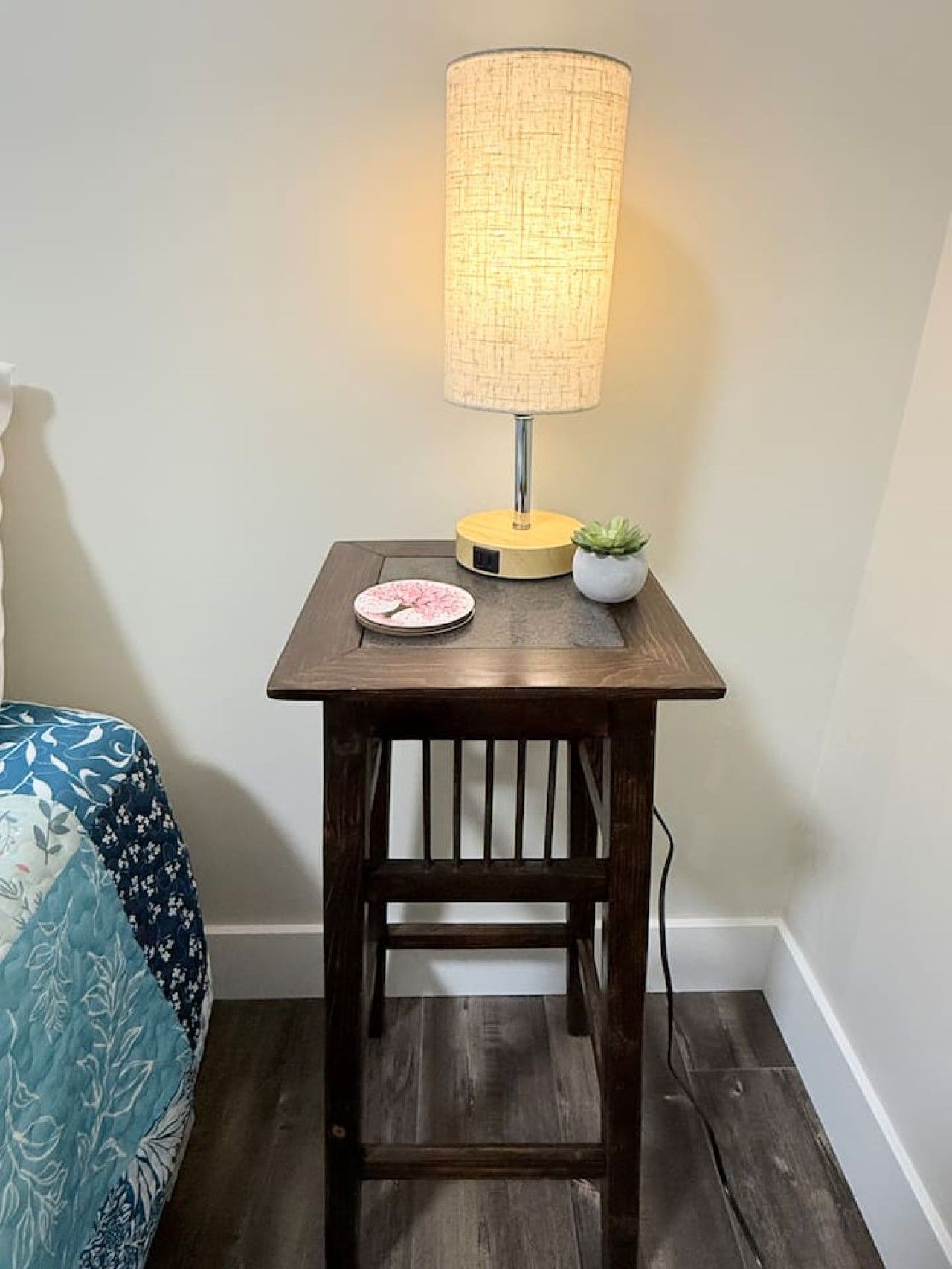 Une petite table en bois, avec une lampe, une assiette et une petite plante.