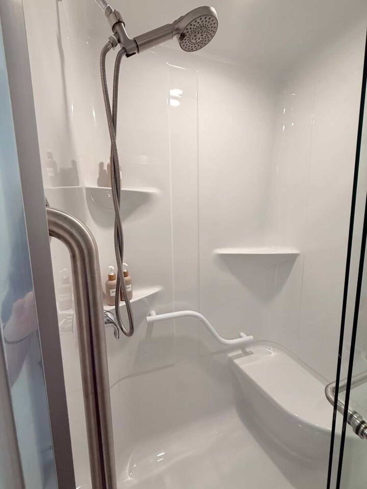 A modern shower enclosure with a handheld showerhead, a handheld shower attachment, and a built-in seat.