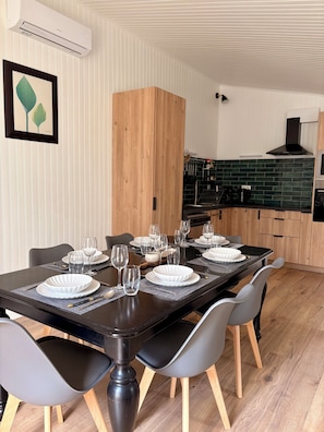 Een eethoek met een rechthoekige tafel voor zes personen, omringd door stoelen, en een keuken met een groene spatwand en houten keukenkastjes.
