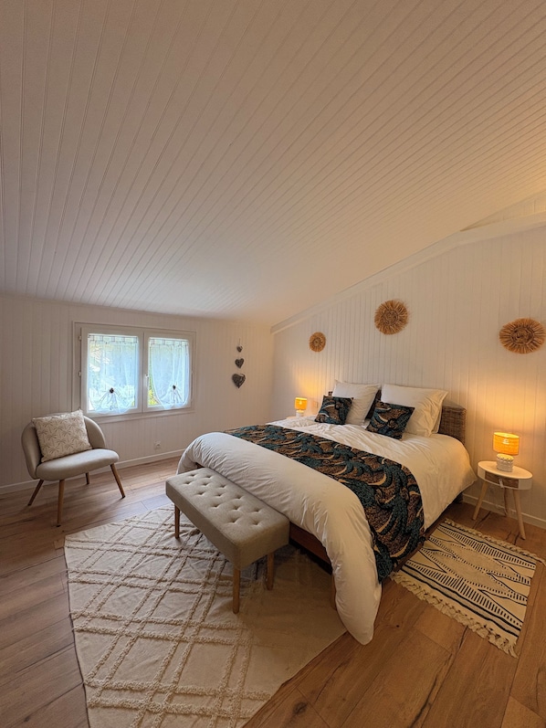 Een slaapkamer met een groot bed, een bankje, een stoel en een nachtkastje met een lamp.