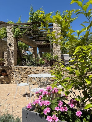 Une terrasse extérieure avec des murs en pierre, une pergola et des chaises en métal.