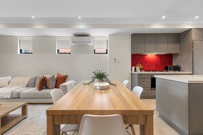 Une cuisine moderne dotée d’un îlot central, un coin repas avec une table et des chaises en bois, et un espace de vie avec un canapé et des coussins.