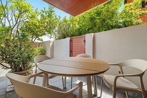 Une terrasse extérieure avec une table ronde et des chaises, entourée de plantes en pot et d’un mur de briques.
