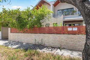 Un bâtiment moderne à deux étages, doté d’une façade en pierre, d’une clôture rouge et d’un arbre au premier plan.