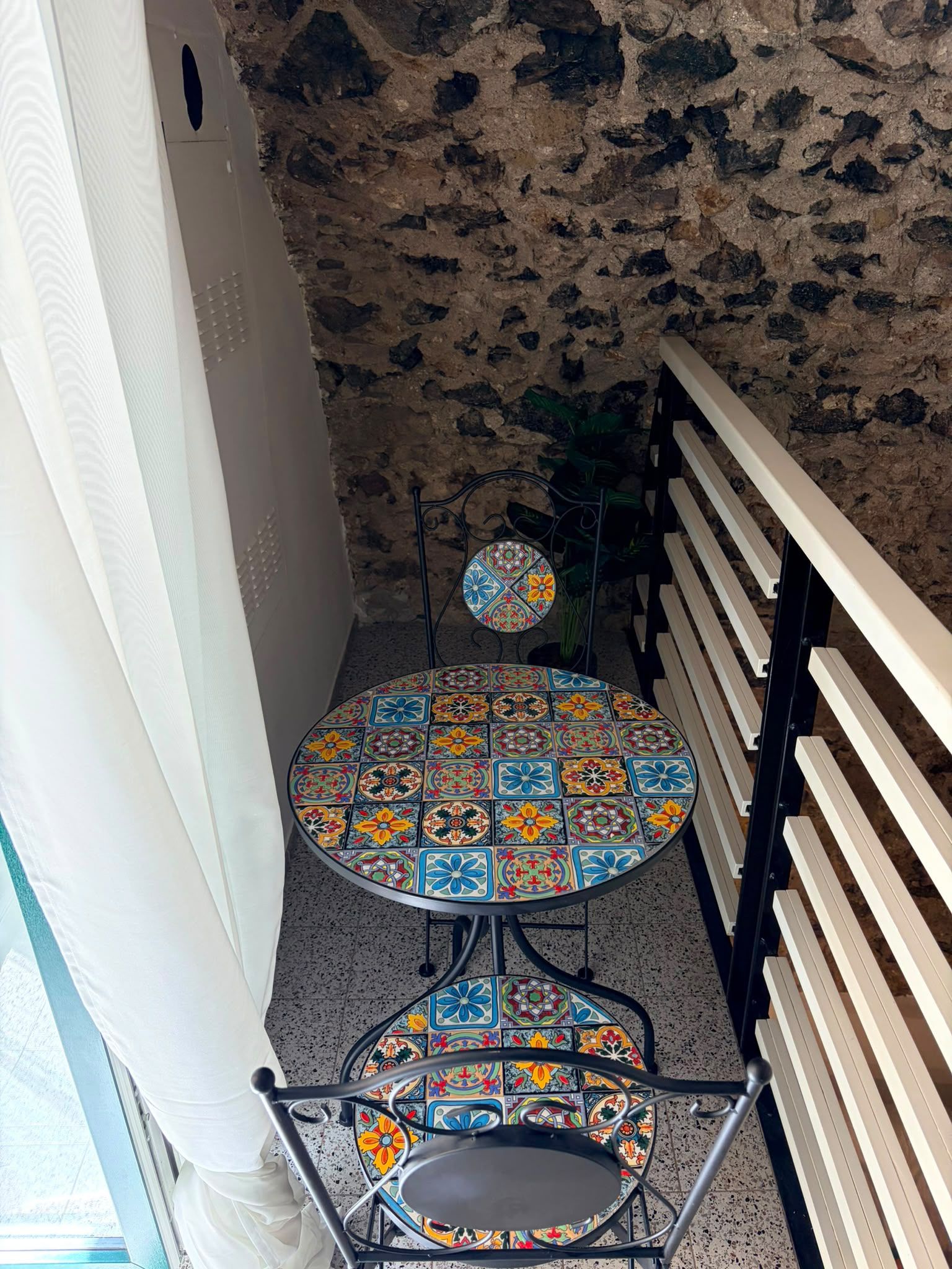 A small, round table with a colorful tiled top, a matching chair, and a bench with a metal frame.