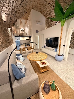 Un intérieur moderne avec un mur en pierre, un coin repas avec une table ronde, un canapé avec des coussins, un téléviseur et une plante en pot.