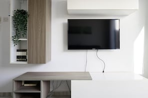 Ein modernes Wohnzimmer mit einem an der Wand befestigten Flachbildfernseher, einer Holzkommode mit einer Pflanze und einem schlichten Tisch.