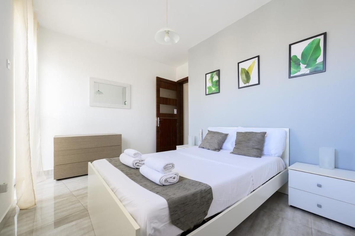 Ein modernes Schlafzimmer mit Bett, Nachttischen, einem Kleiderschrank und Bildern an der Wand.
