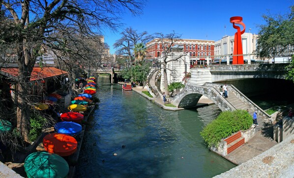 A canal with colorful umbrellas lining the path, a stone bridge, and a building with classical architecture in the background. - Accessible 1BR City View Suite w/ Free Breakfast (San Antonio)