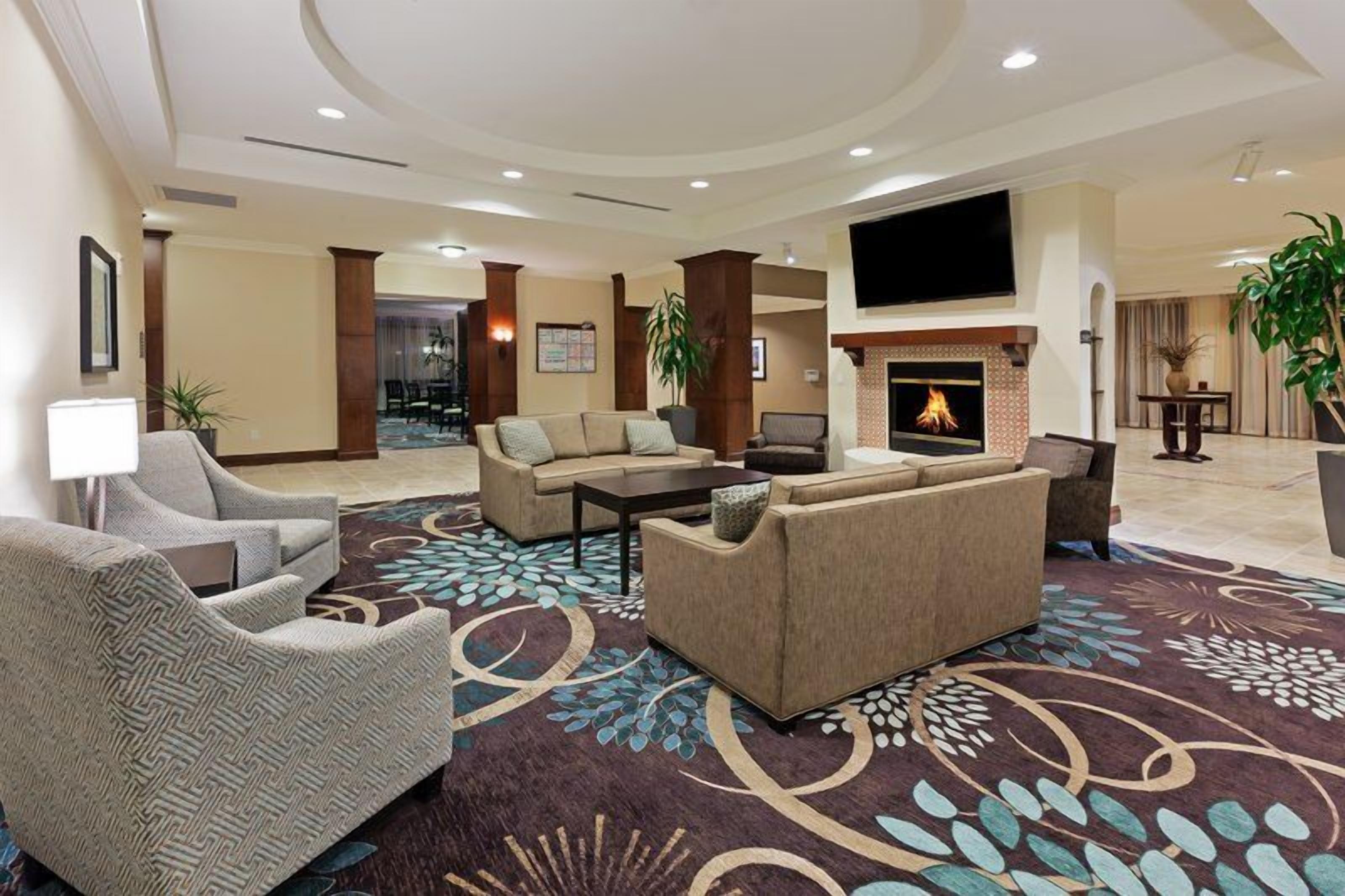 Eine Hotelhalle mit Kamin, Sofas, Sesseln und einem großen Fernseher.