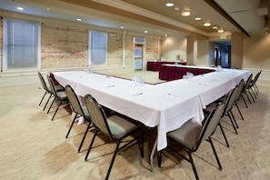 Une salle de conférence avec une longue table, des chaises et un mur en briques.