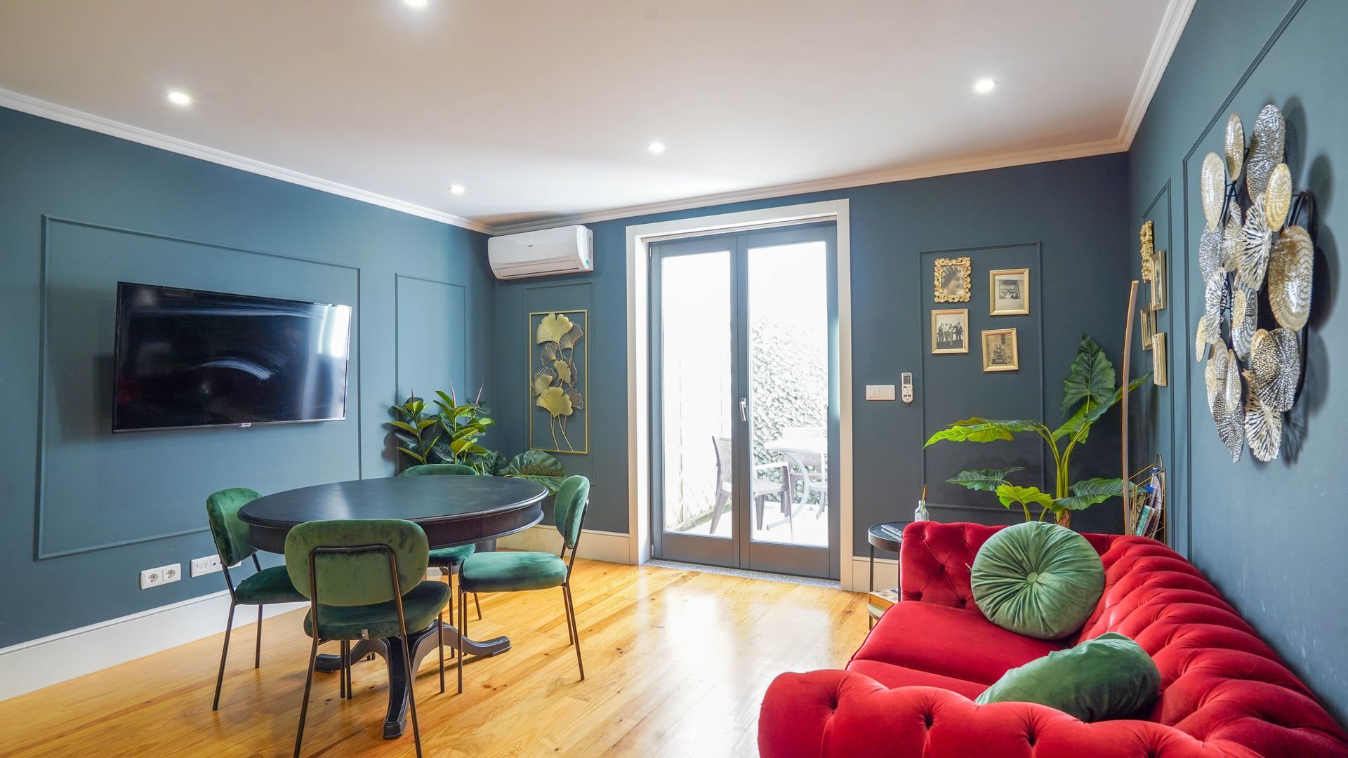 A modern living room with a red sofa, green chairs, a dining table, and a TV mounted on the wall.