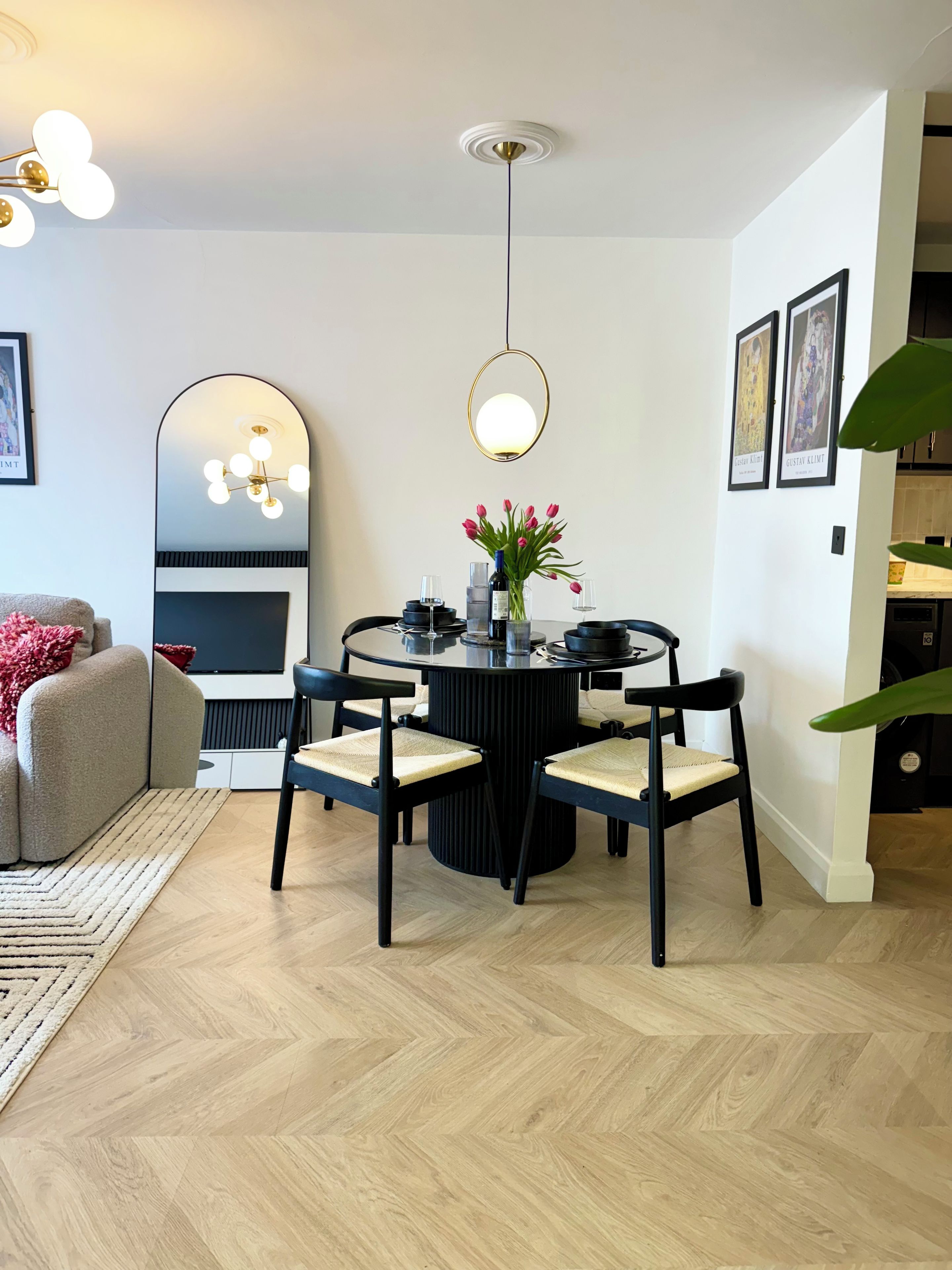 Ein Essbereich mit einem runden Tisch, Stühlen, einer Blumenvase und einer modernen Pendelleuchte.