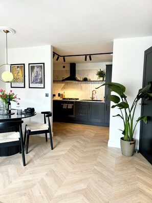 A modern kitchen with a herringbone floor, a dining area with a round table and chairs, and two framed artworks on the wall.