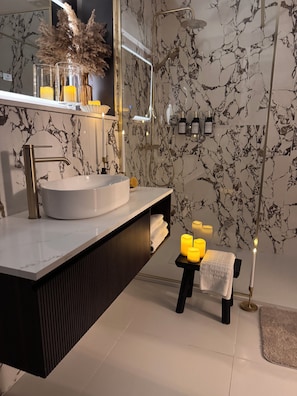 Un baño moderno con pared de mármol, un lavabo redondo, un espejo y un perchero para toallas.