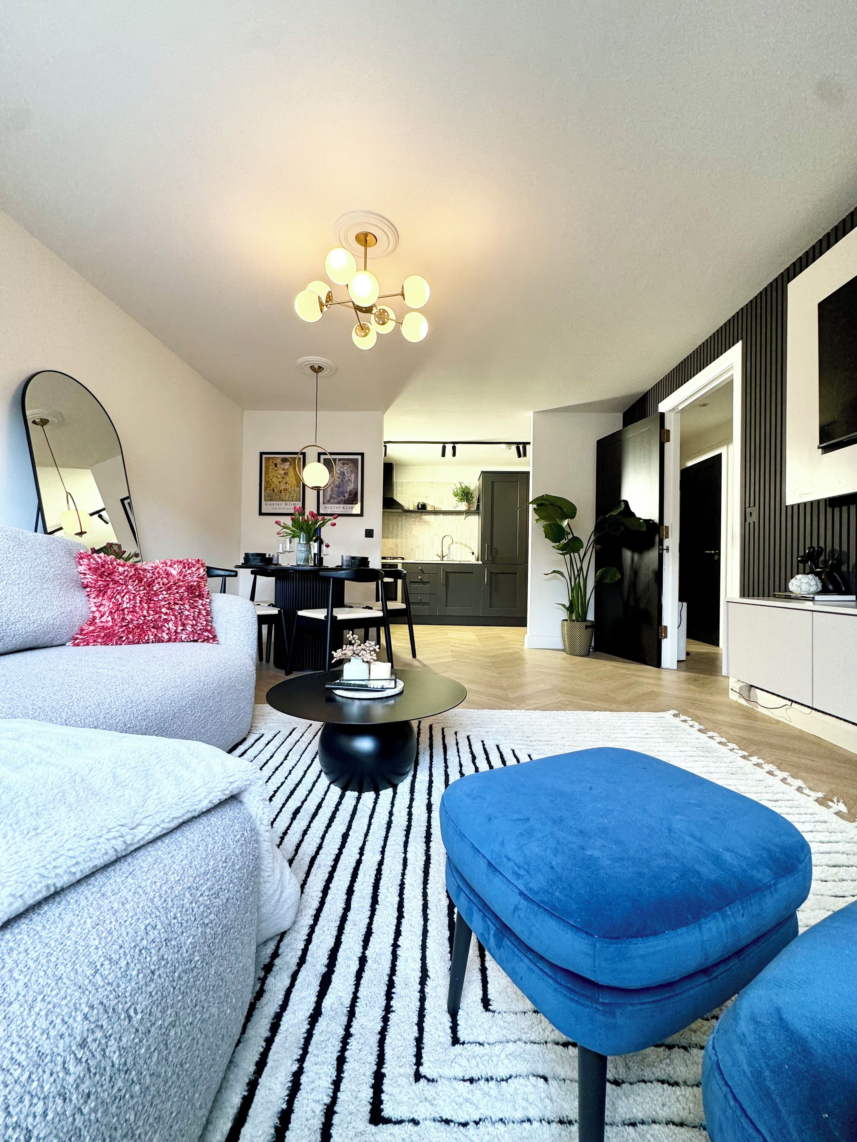 Ein modernes Wohnzimmer mit einer Couch, einem Hocker und einem Essbereich mit Stühlen und einem Tisch.