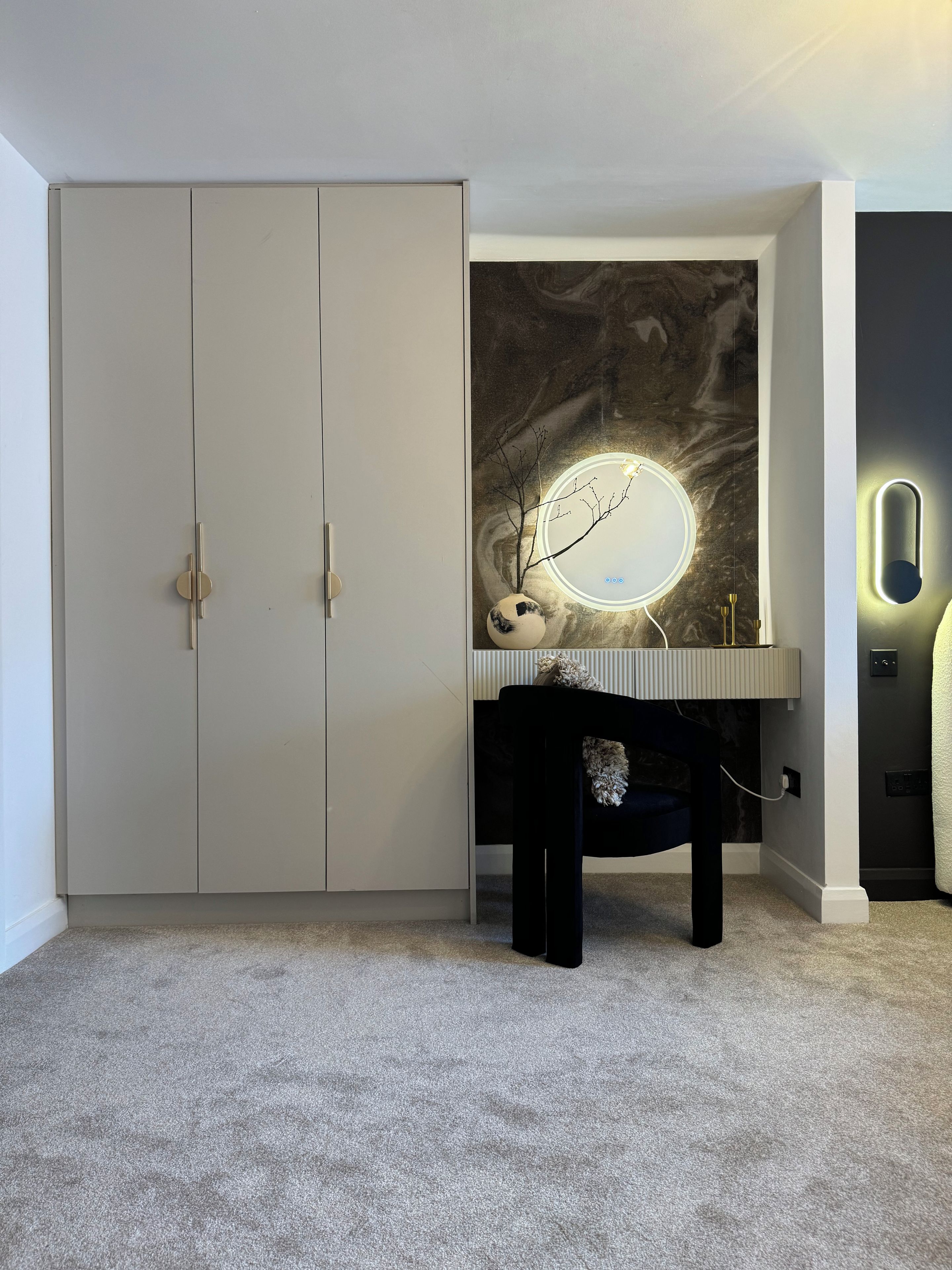 Ein Schlafzimmer mit Kleiderschrank, Schminktisch mit Spiegel und einer Wandleuchte.