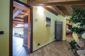 Un pasillo con piso de madera, una puerta con un panel decorativo y una lámpara fijada a la pared.
