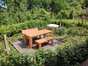 Ein Holztisch mit Bank auf einem befestigten Bereich, umgeben von üppigem Grün.