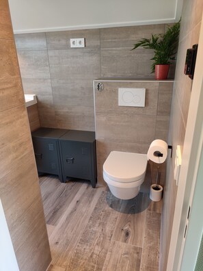 Ein modernes Badezimmer mit Toilette, Bidet, Stauraumschrank und einer Topfpflanze.